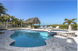 Upper Keys luxury homes for sale slide show. Back yard with pool, tiki thatch roof, and the ocean in the background.